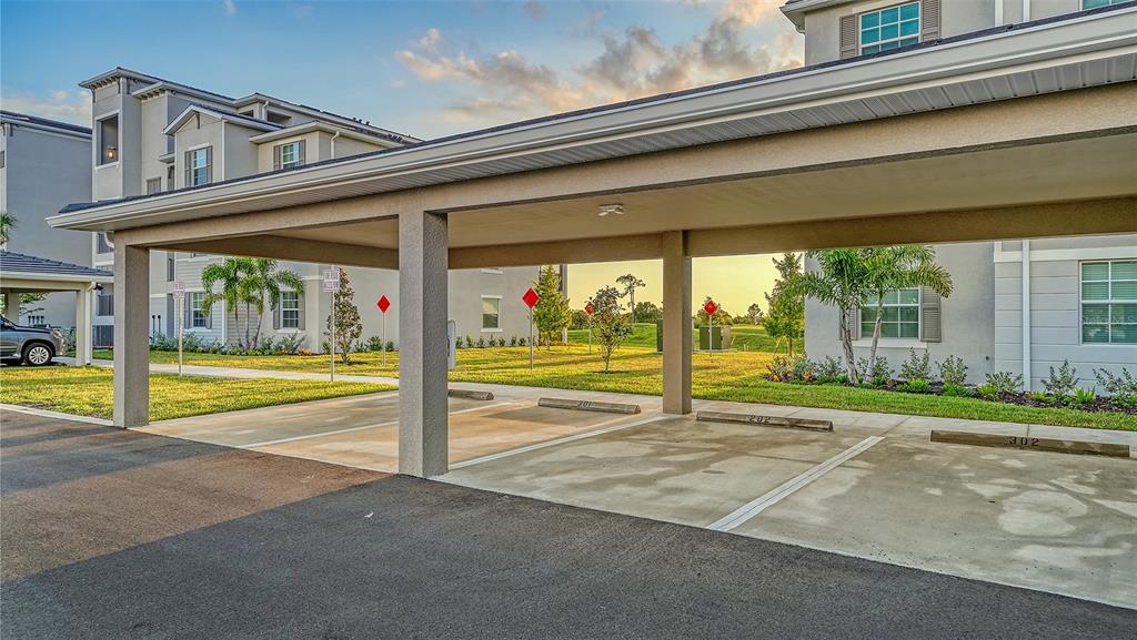 A covered parking structure with numbered spaces sits in front of a multi-story apartment building — 17655 OPAL SAND DRIVE UNIT 301, VENICE, FL