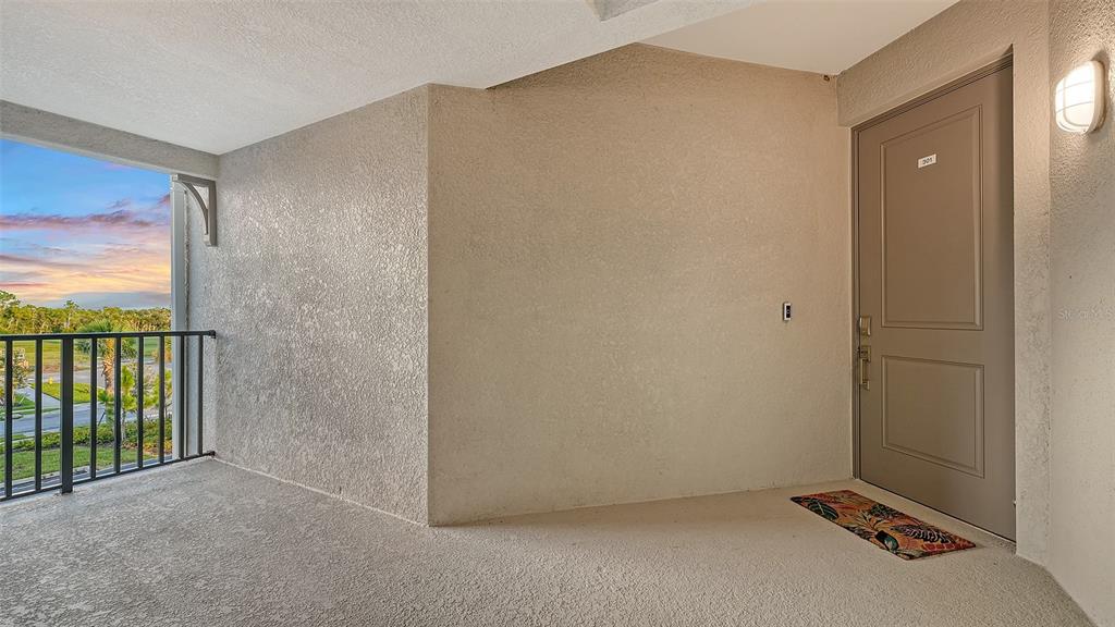 An apartment entrance with a beige door, textured walls, and a balcony overlooking a landscape — 17655 OPAL SAND DRIVE UNIT 301, VENICE, FL