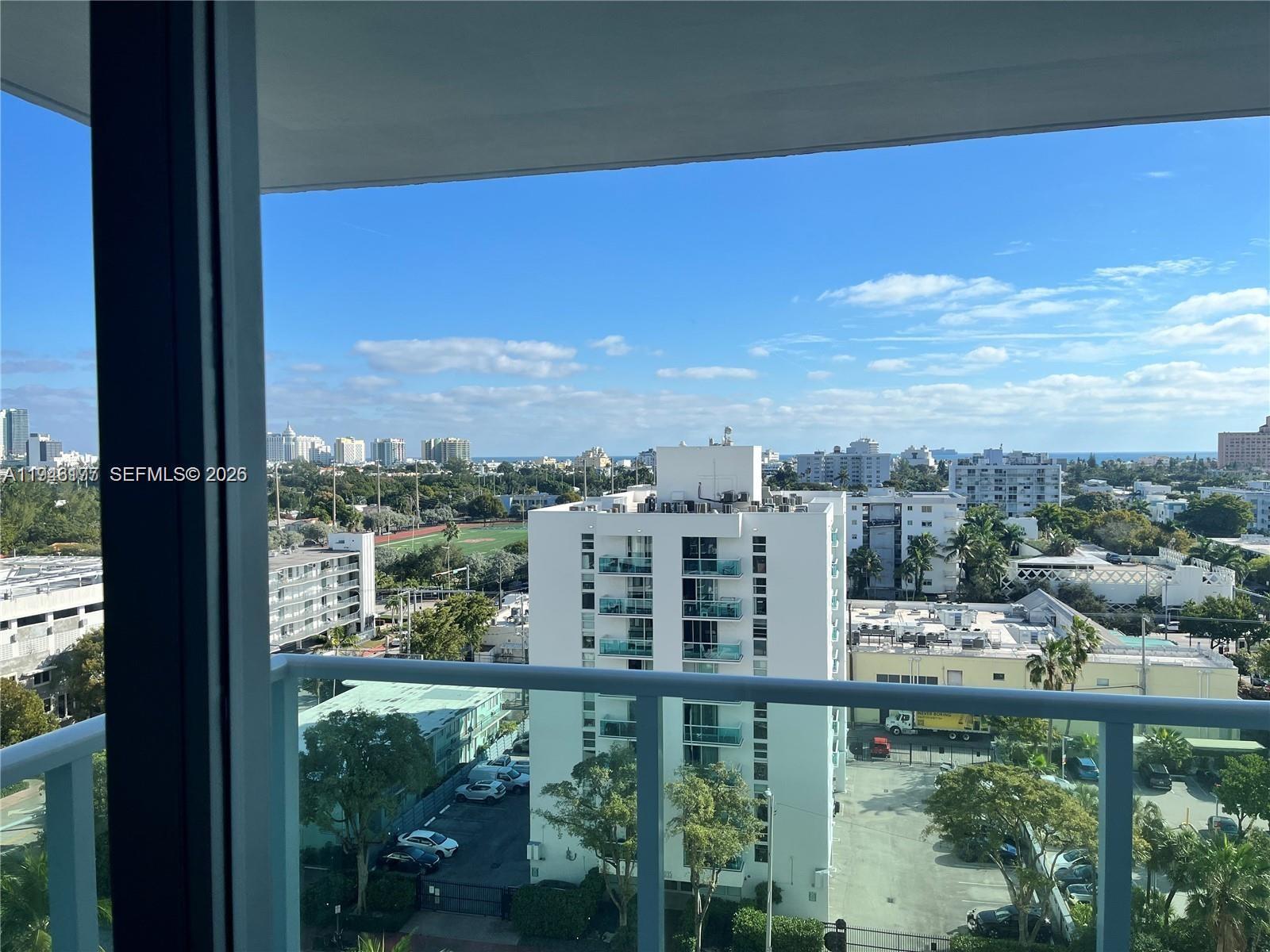 A balcony view overlooks a city skyline, a white apartment building, and a green field — 1000 West Ave # 1006, Miami Beach FL 33139, MIAMI BEACH, FL