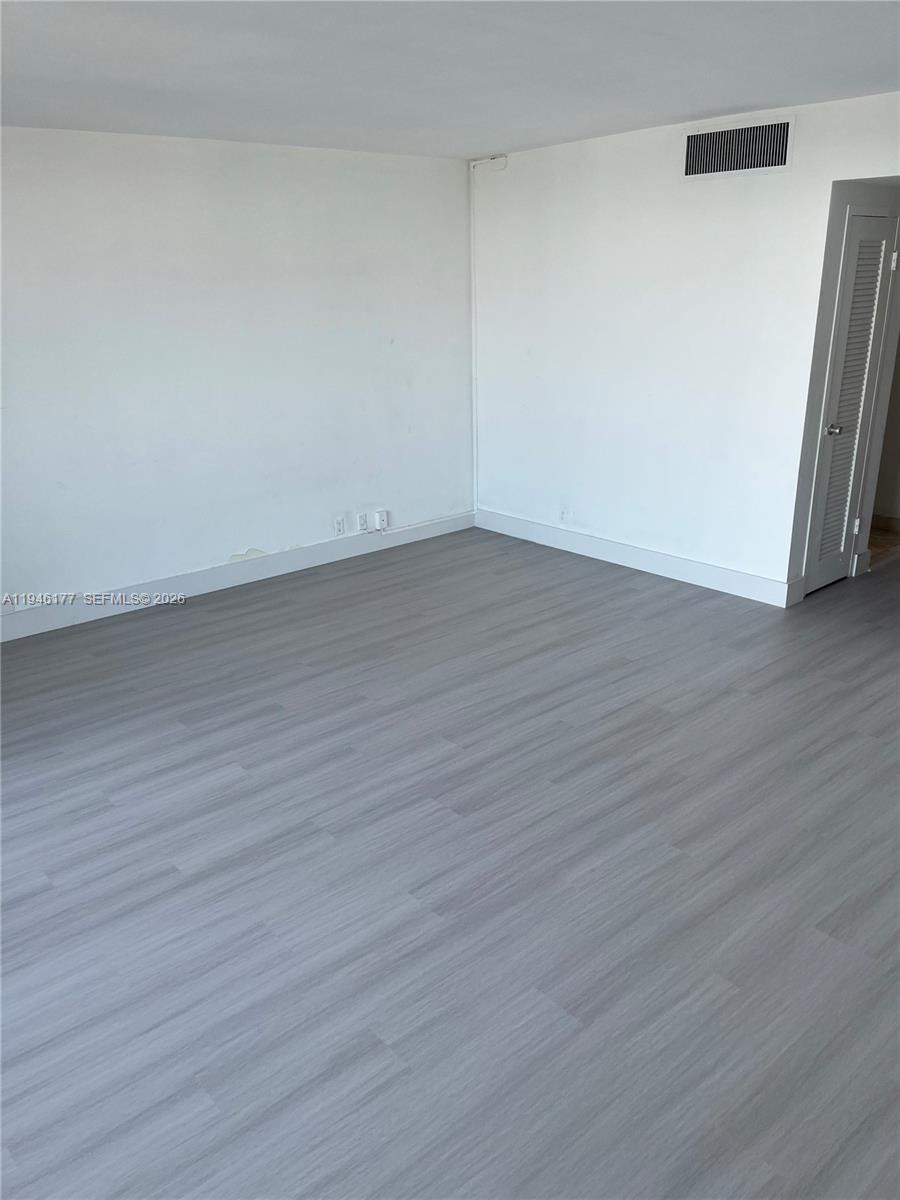 An empty room features white walls, gray wood-look flooring, and a louvered closet door — 1000 West Ave # 1006, Miami Beach FL 33139, MIAMI BEACH, FL