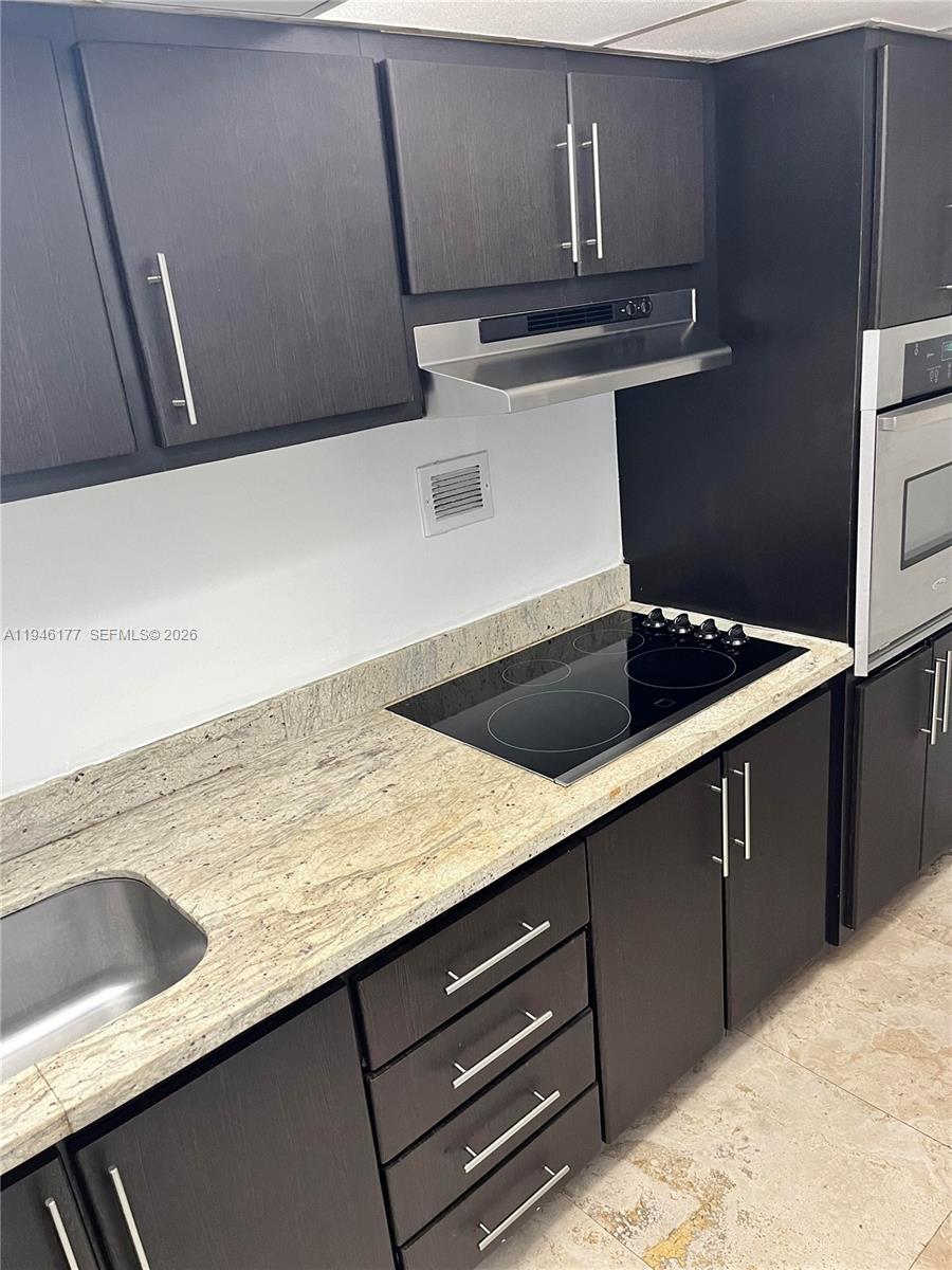 A kitchen features dark wood cabinets, a granite countertop, and a black electric cooktop — 1000 West Ave # 1006, Miami Beach FL 33139, MIAMI BEACH, FL