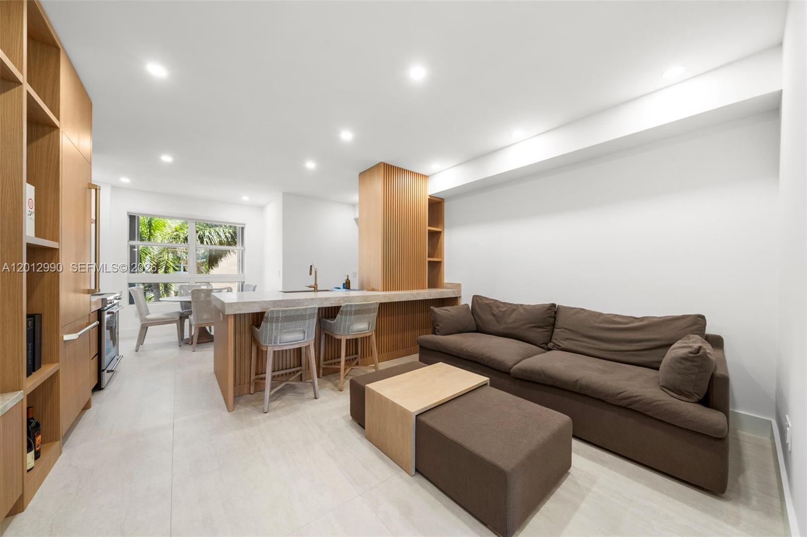 A modern open-plan living area features a kitchen island, wooden cabinetry, and a brown sofa — 701 Crandon Blvd # 401, Key Biscayne FL 33149, KEY BISCAYNE, FL