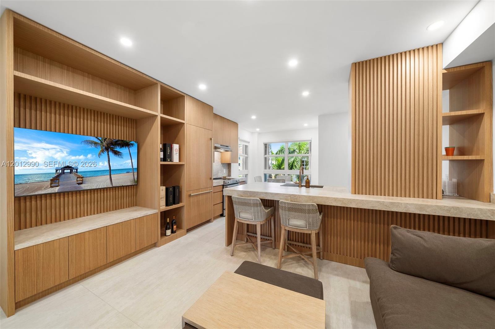 A modern kitchen and living area feature light wood cabinetry, slatted wall panels, and stone countertops — 701 Crandon Blvd # 401, Key Biscayne FL 33149, KEY BISCAYNE, FL