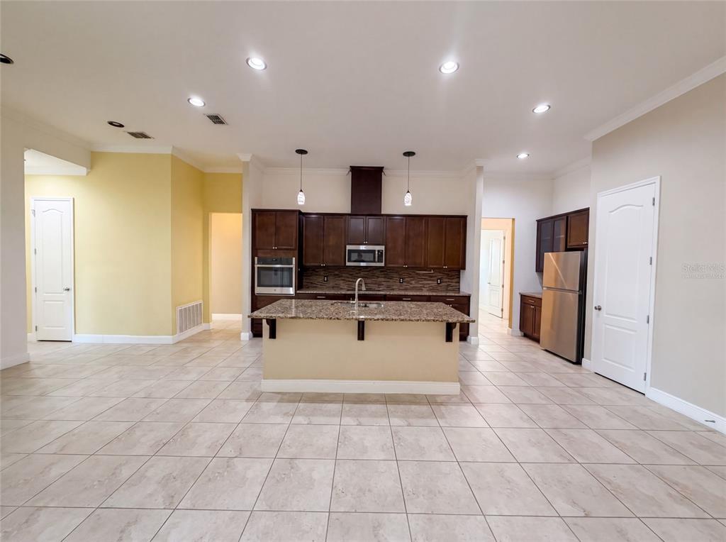A kitchen features dark wood cabinets, granite countertops, a central island, and tile flooring — 918 BLACKTHORN DRIVE, APOPKA, FL