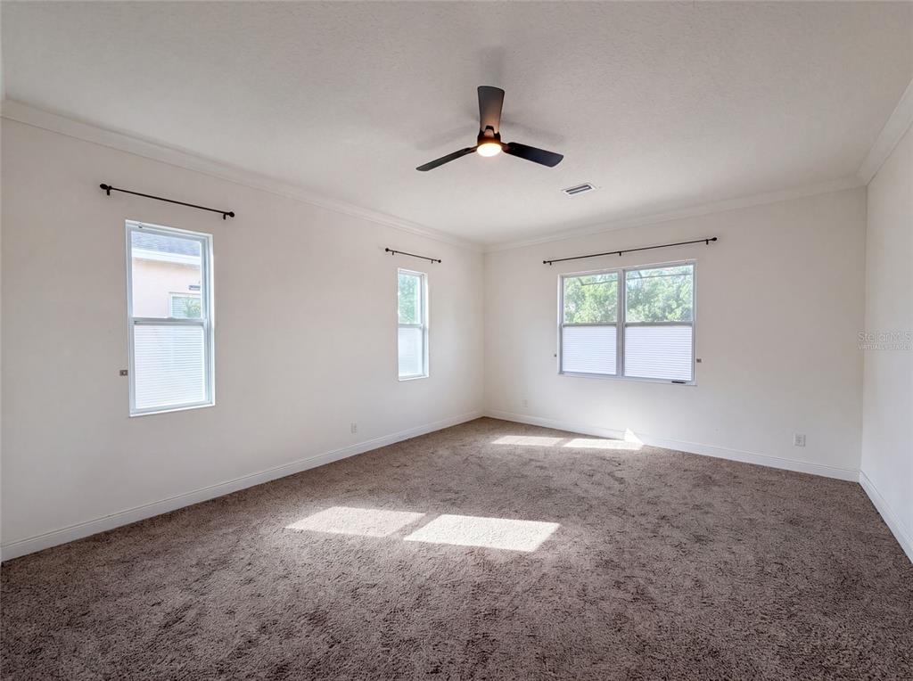 An empty bedroom with beige carpet, white walls, three windows, and a ceiling fan — 918 BLACKTHORN DRIVE, APOPKA, FL