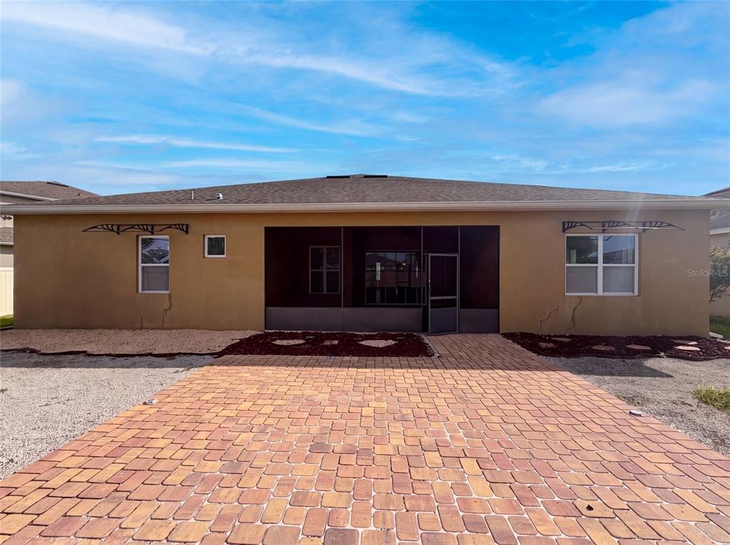 The rear exterior of a house features a paved patio and a screened-in porch area — 918 BLACKTHORN DRIVE, APOPKA, FL