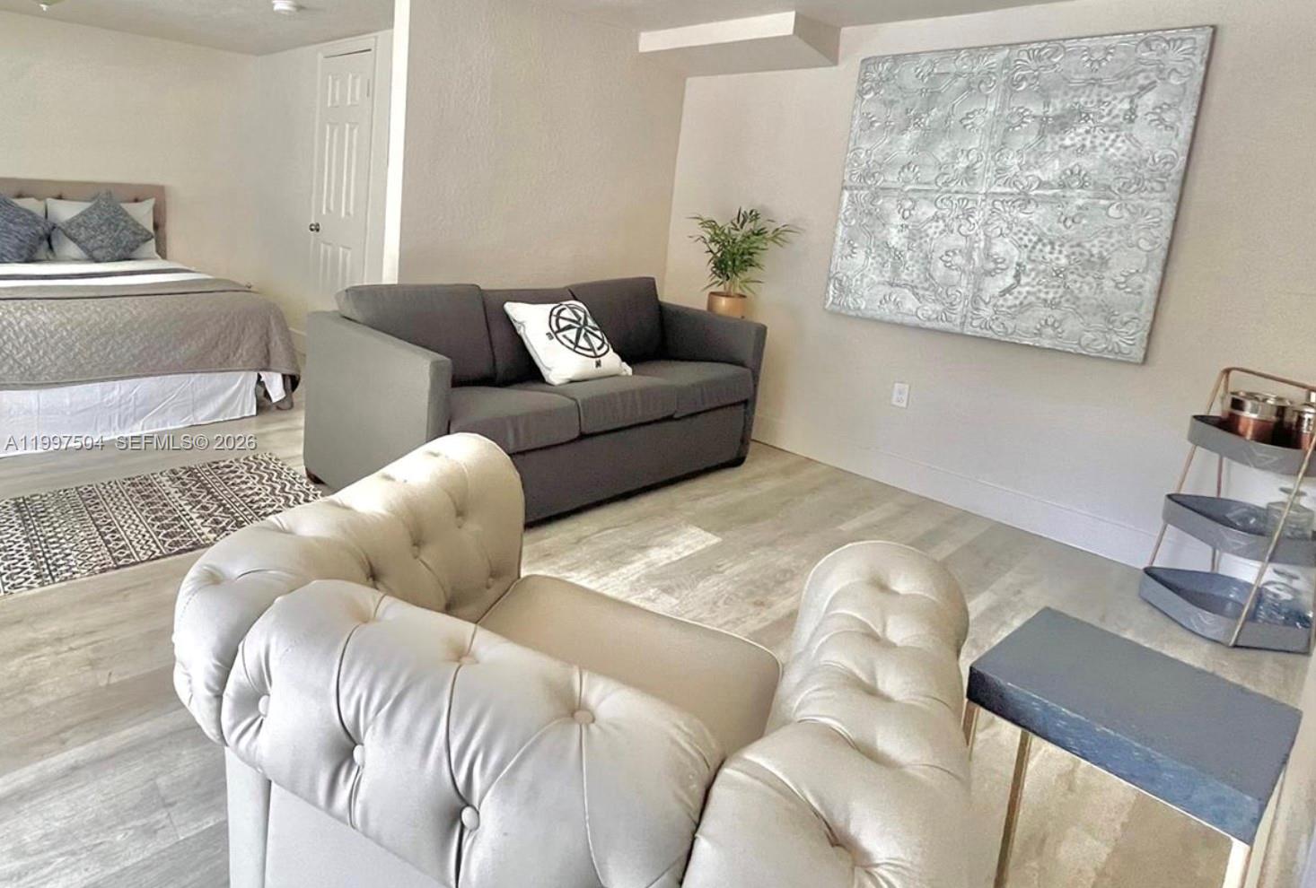 A furnished room features a bed, a gray sofa, a tufted chair, and wall art — 21 NE 53 ST, Miami FL 33137, MIAMI, FL