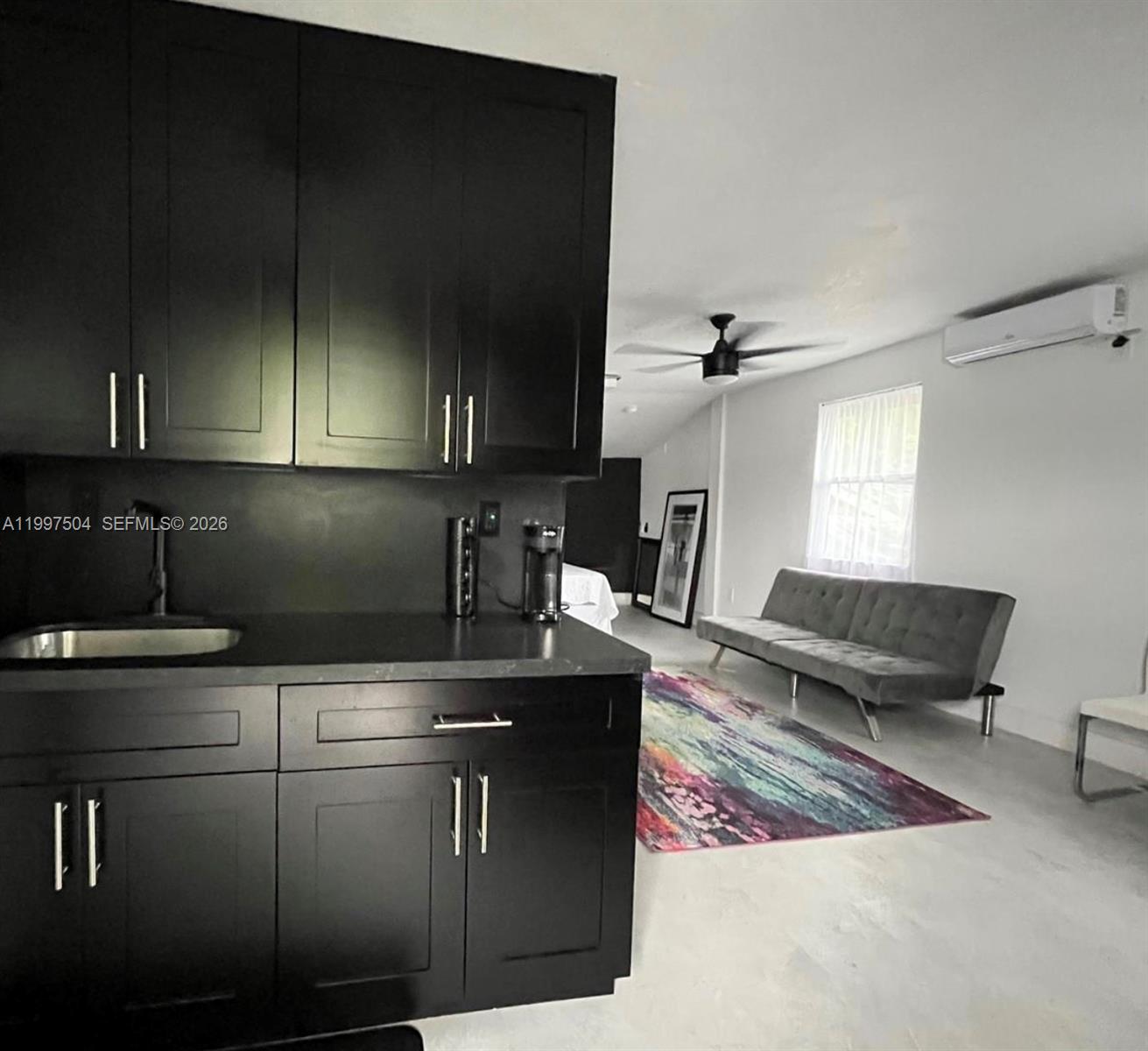 A kitchen with black cabinets and a sink overlooks a living area with a sofa — 21 NE 53 ST, Miami FL 33137, MIAMI, FL