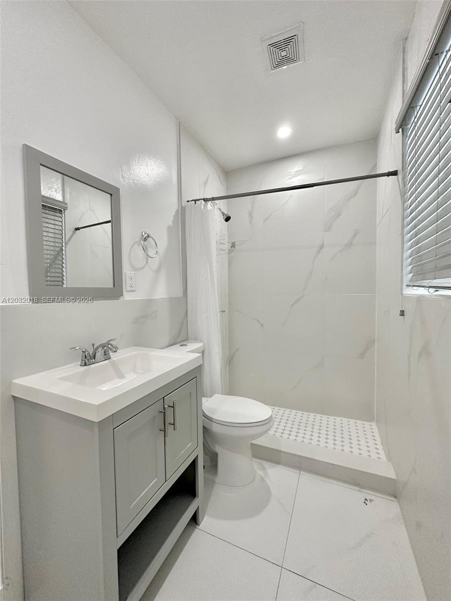 A modern bathroom features a gray vanity, a white toilet, and a tiled walk-in shower — 156 NW 62nd St # 1, Miami FL 33150, MIAMI, FL