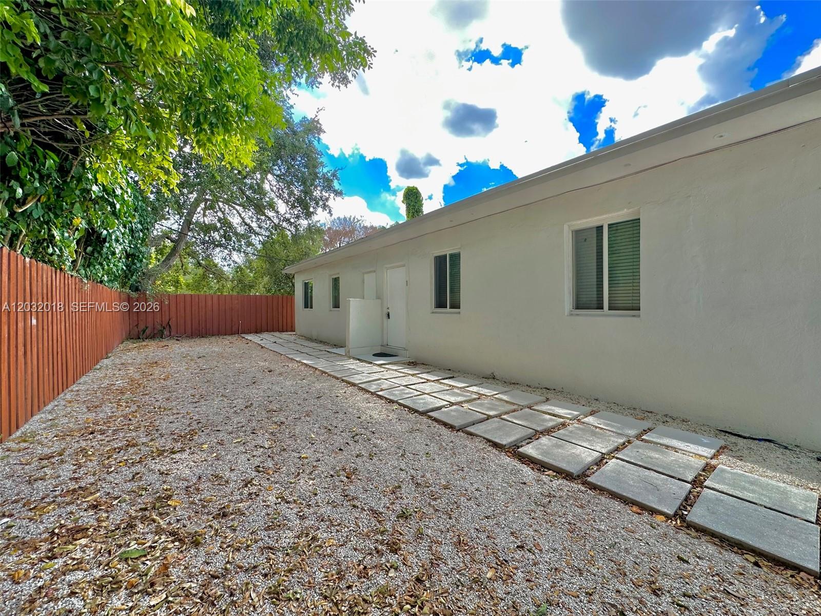 A white exterior wall features a doorway and windows alongside a gravel yard with pavers — 156 NW 62nd St # 1, Miami FL 33150, MIAMI, FL