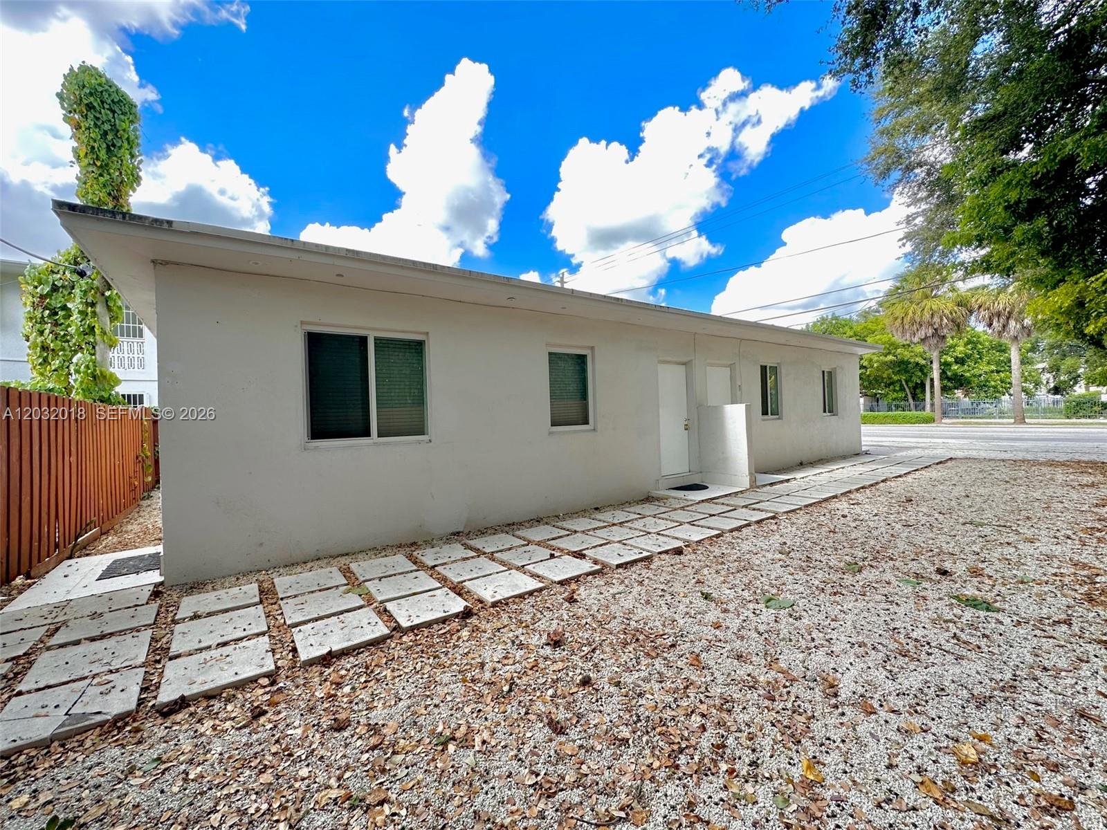 The exterior of a white, single-story building features a gravel yard and concrete paver walkway — 156 NW 62nd St # 1, Miami FL 33150, MIAMI, FL