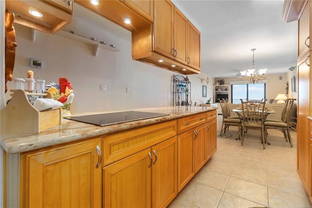 A kitchen with light wood cabinets and granite countertops overlooks a dining and living area — 4201 S ATLANTIC AVENUE UNIT 409, NEW SMYRNA BEACH, FL