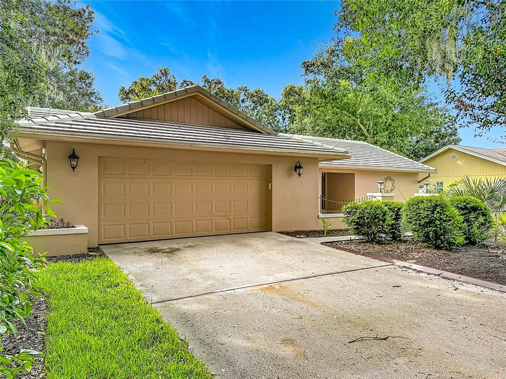 A tan single-story house features a two-car garage, a concrete driveway, and surrounding landscaping — 3097 EDGEMOOR DRIVE, PALM HARBOR, FL