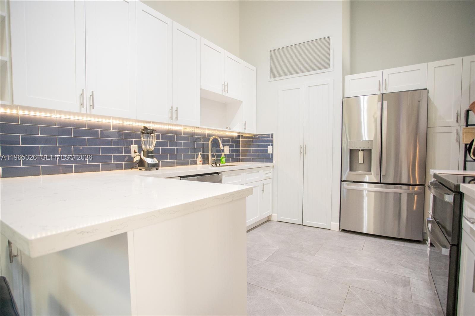 A modern kitchen features white cabinets, a blue subway tile backsplash, and stainless steel appliances — 523 Leslie Dr, Hallandale Beach FL 33009, HALLANDALE BEACH, FL