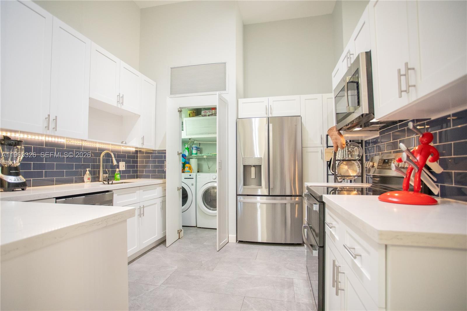 A modern kitchen features white cabinets, stainless steel appliances, blue subway tile, and a laundry closet — 523 Leslie Dr, Hallandale Beach FL 33009, HALLANDALE BEACH, FL