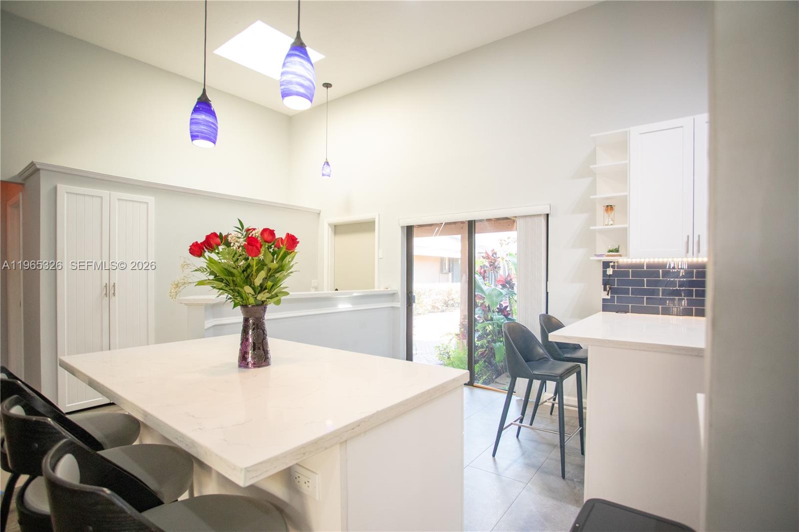 A bright kitchen features a white island, blue pendant lights, and a sliding glass door — 523 Leslie Dr, Hallandale Beach FL 33009, HALLANDALE BEACH, FL