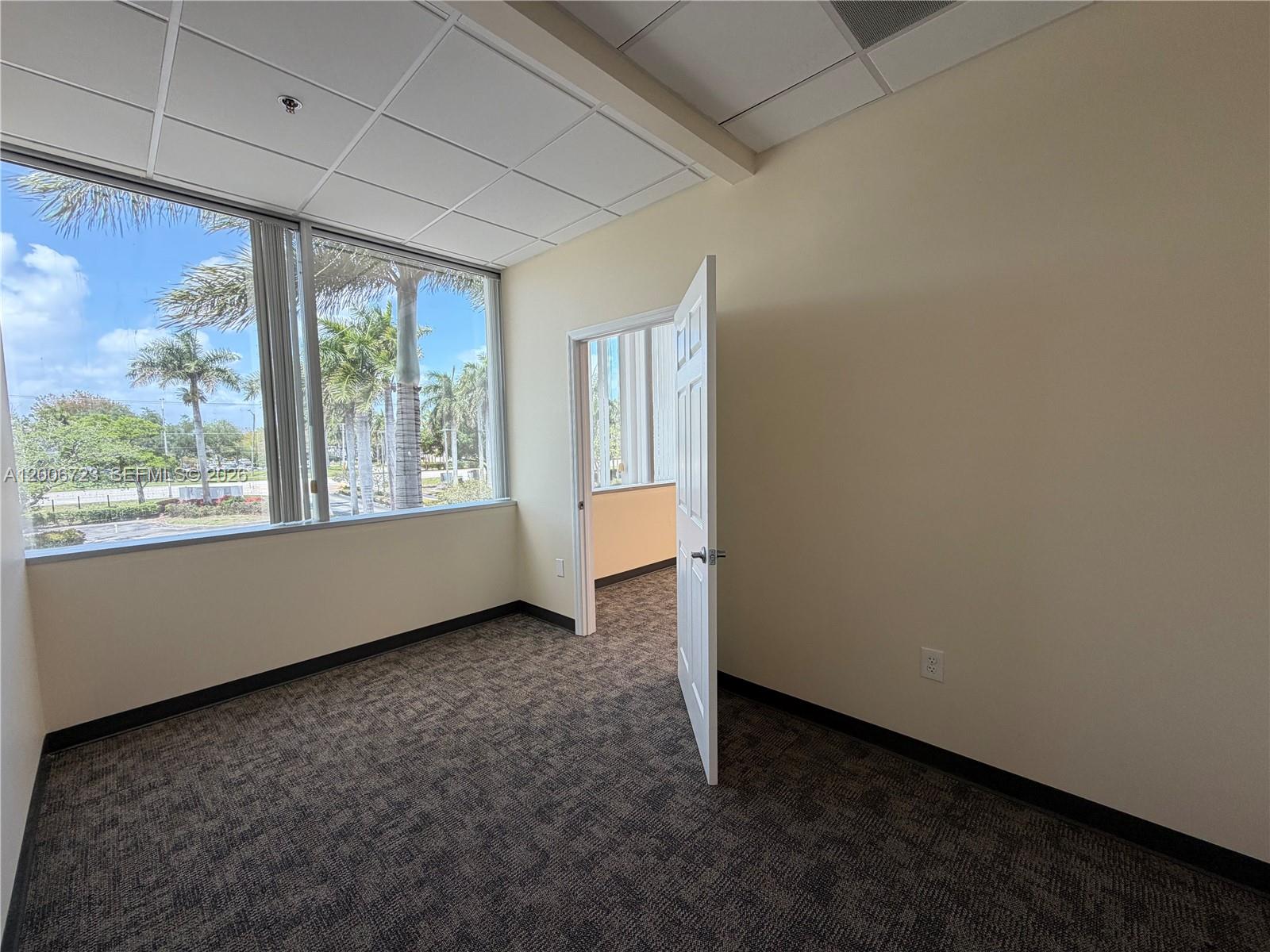 An empty office features gray carpet, beige walls, a white door, and large windows — 4400 W Sample Rd # 250, Coconut Creek FL 33073, COCONUT CREEK, FL