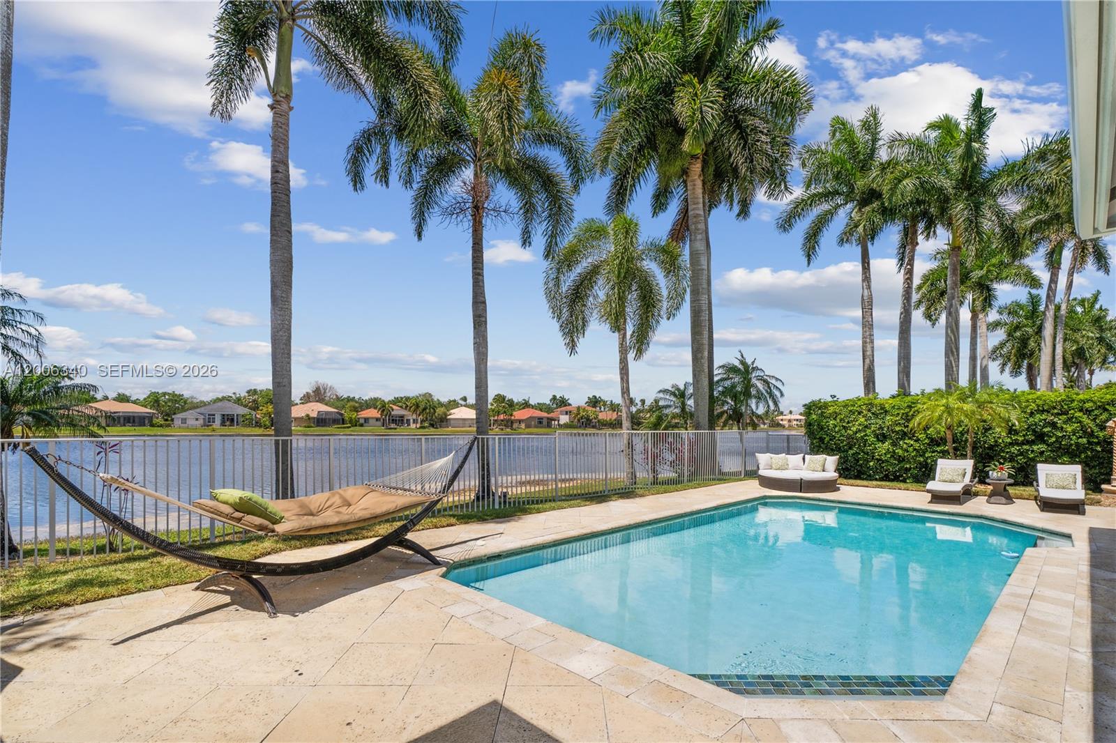 A swimming pool and hammock sit on a patio overlooking a lake with palm trees — 2942 Medinah, Weston FL 33332, WESTON, FL