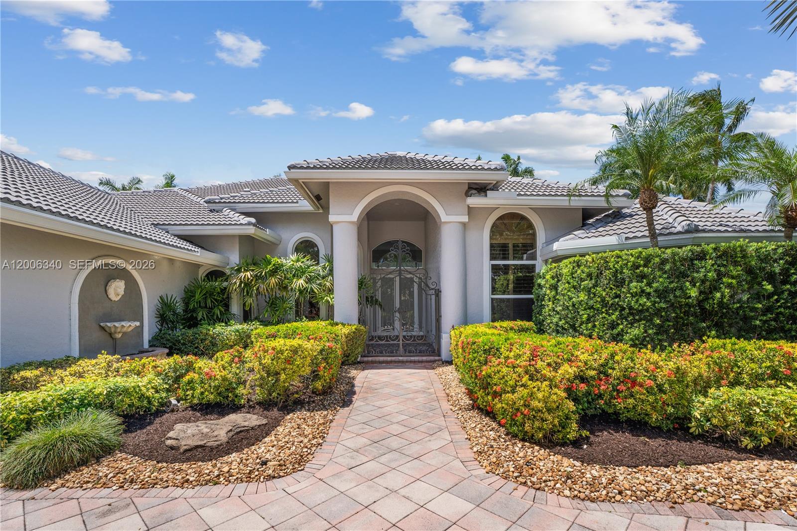 The exterior of a single-story house features a tiled roof, arched entryway, and landscaped garden — 2942 Medinah, Weston FL 33332, WESTON, FL