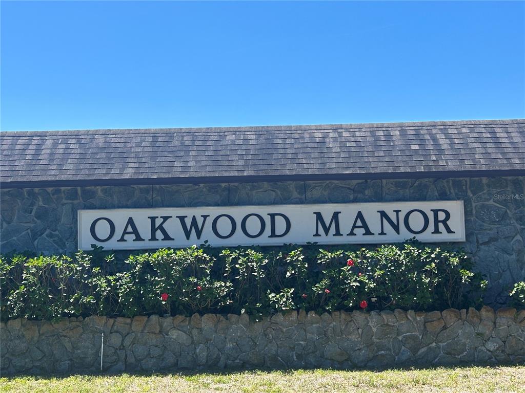 A stone wall features a sign reading Oakwood Manor beneath a shingled roof — 3221 SWEET GUM TERRACE, SARASOTA, FL