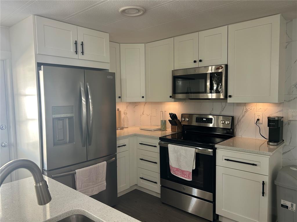 A kitchen features white cabinets, stainless steel appliances, and a marble-patterned backsplash — 3221 SWEET GUM TERRACE, SARASOTA, FL