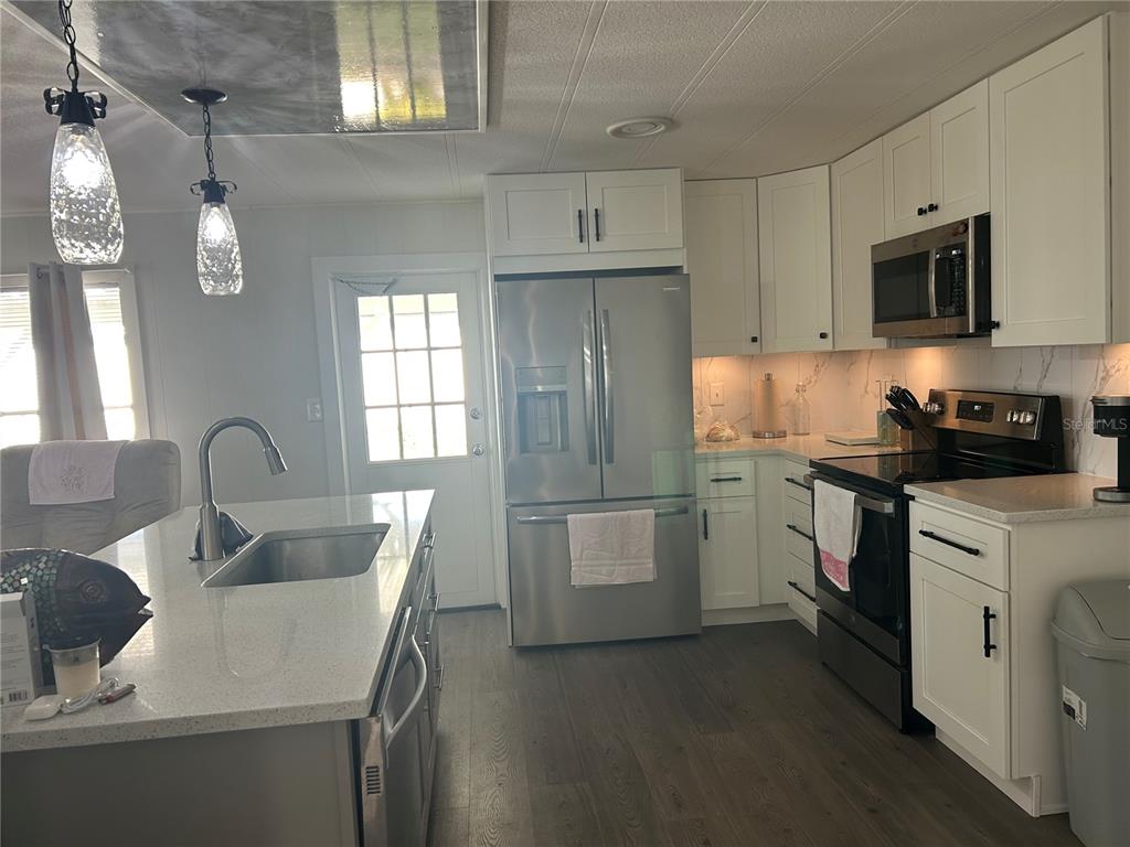 A modern kitchen features white cabinets, stainless steel appliances, and a quartz-topped island — 3221 SWEET GUM TERRACE, SARASOTA, FL