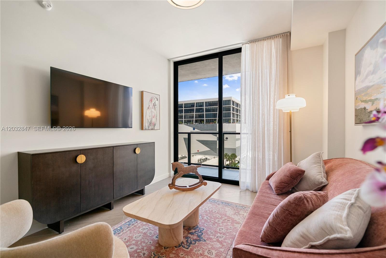 A living room features a dark media console, a pink sofa, and a balcony view — 2700 NW 2ND AVE # 728, Miami FL 33127, MIAMI, FL