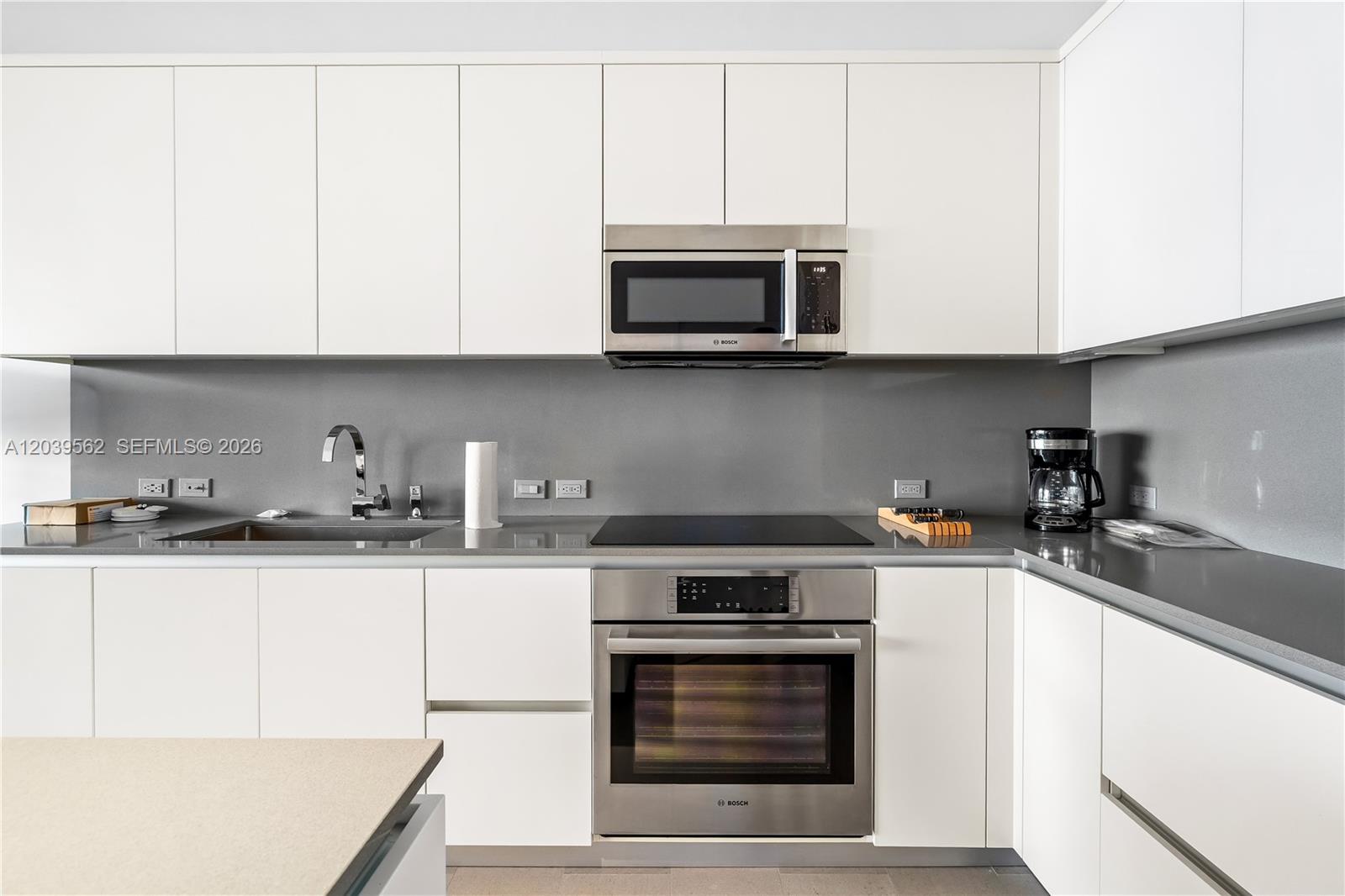 A modern kitchen features white flat-panel cabinets, stainless steel appliances, and a gray backsplash — 88 SW 7th St # 1006, Miami FL 33130, MIAMI, FL