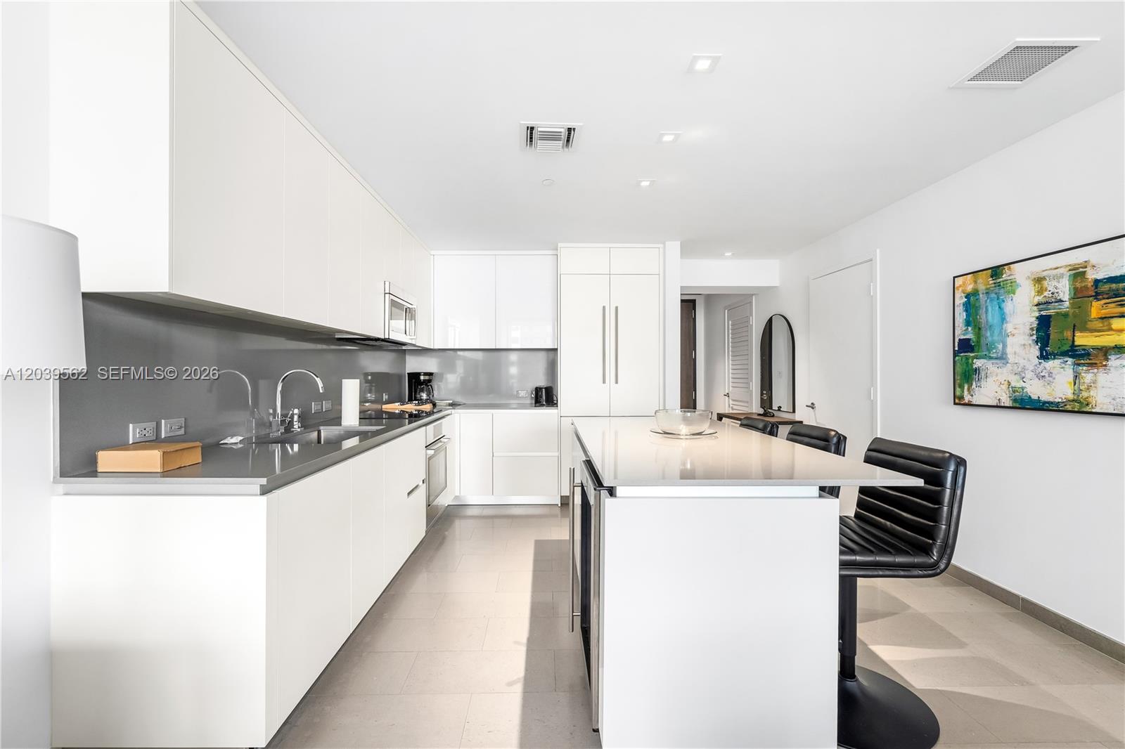 A modern kitchen features white cabinetry, a gray backsplash, and a central island with seating — 88 SW 7th St # 1006, Miami FL 33130, MIAMI, FL