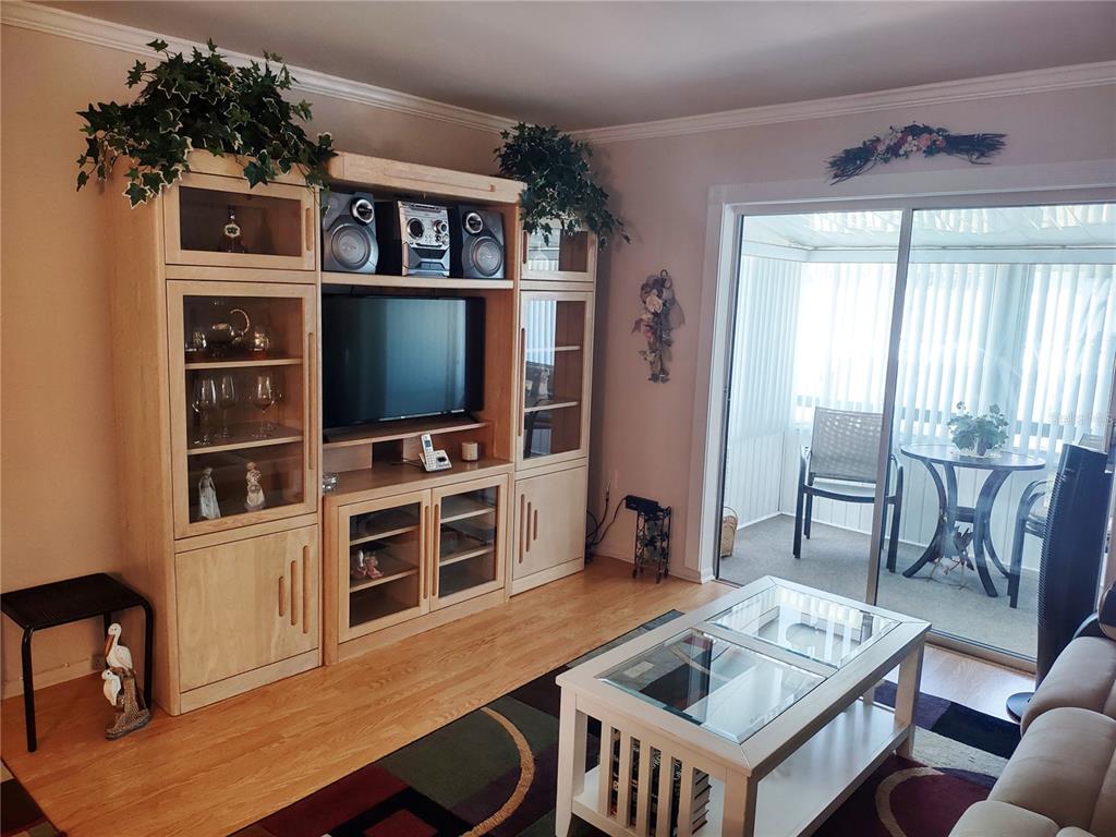 A living room features a large wooden entertainment center, a glass-topped coffee table, and sliding doors — 1815 SUNNY DRIVE UNIT E21, BRADENTON, FL
