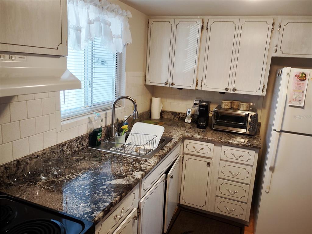A kitchen features white cabinets, granite countertops, a stainless steel sink, and white appliances — 1815 SUNNY DRIVE UNIT E21, BRADENTON, FL