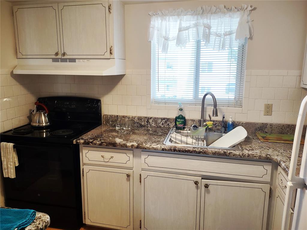 A kitchen features white cabinets, granite countertops, a black stove, and a stainless steel sink — 1815 SUNNY DRIVE UNIT E21, BRADENTON, FL
