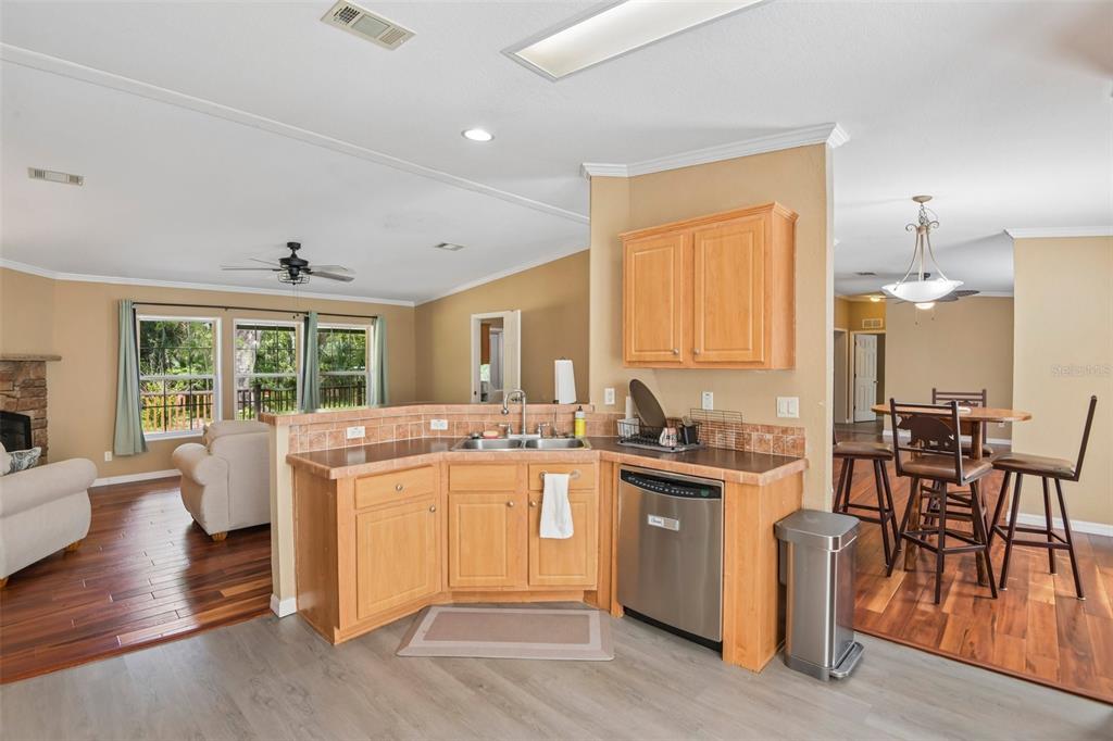 A kitchen with light wood cabinets, tile countertops, and stainless steel appliances overlooks a living area — 6221 EMERSON ROAD, BROOKSVILLE, FL
