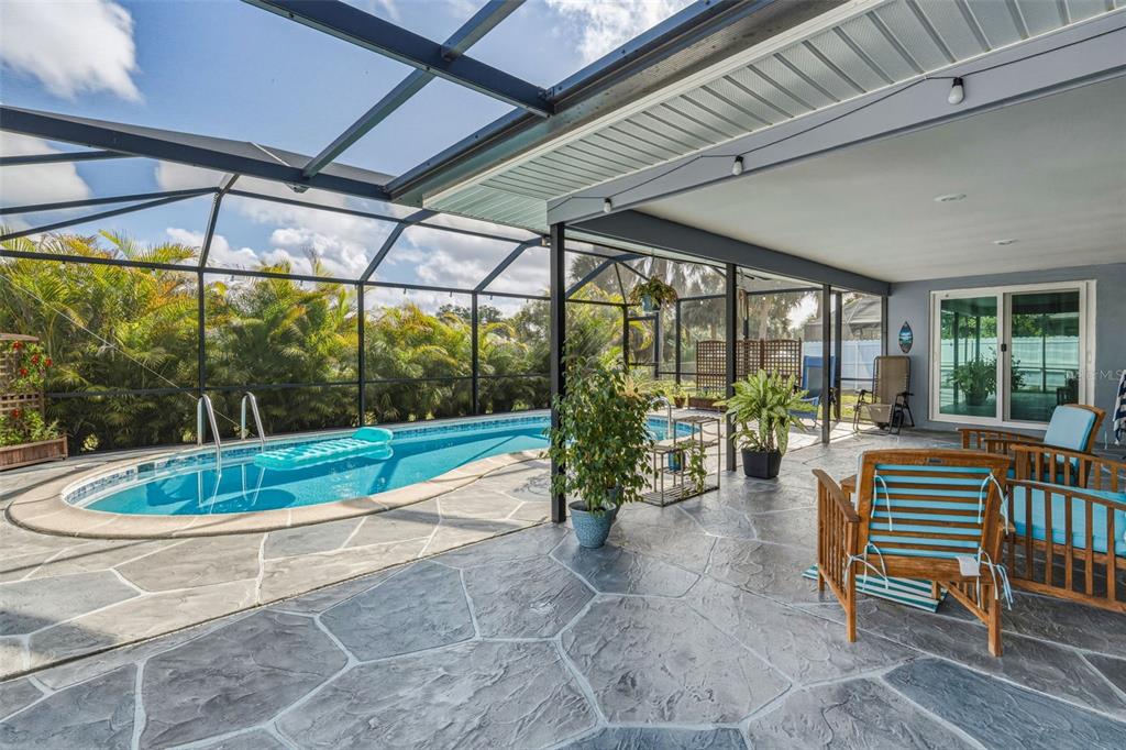 A screened-in patio features a swimming pool, stone-patterned concrete flooring, and outdoor furniture — 2440 AUBURN BOULEVARD, PORT CHARLOTTE, FL