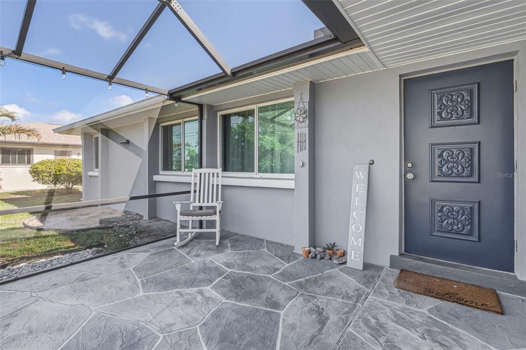 A covered porch features gray stone-patterned flooring, a white rocking chair, and a blue door — 2440 AUBURN BOULEVARD, PORT CHARLOTTE, FL