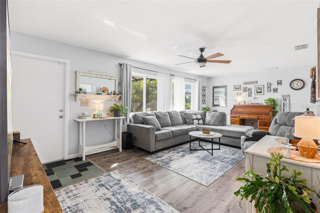 A living room features a gray sectional sofa, wood-look flooring, and a ceiling fan — 2440 AUBURN BOULEVARD, PORT CHARLOTTE, FL