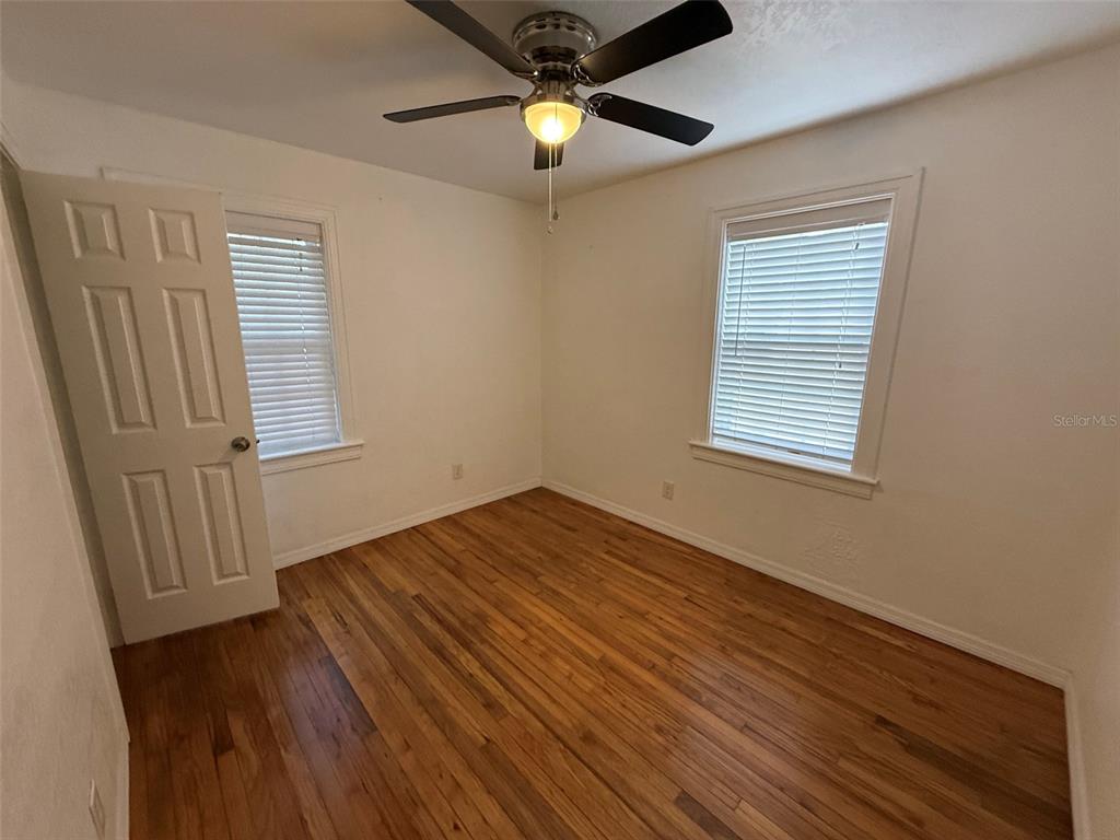 An empty bedroom features hardwood floors, a ceiling fan, and two windows with white blinds — 5521 5TH AVENUE N, ST PETERSBURG, FL