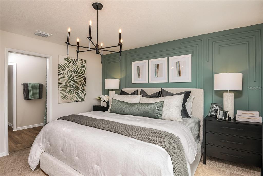 A bedroom features a green paneled accent wall, a chandelier, and a white upholstered bed — 9864 PELICAN COAST DRIVE, DADE CITY, FL