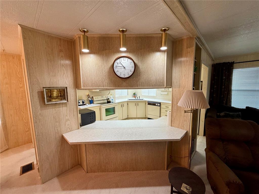 A kitchen features off-white cabinets, a white electric range, a corner sink, and wood-paneled walls — 6571 NE 1ST PLACE, OCALA, FL