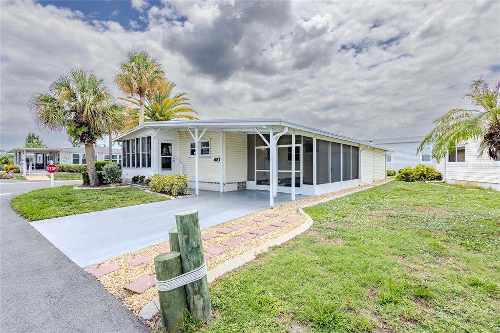 A light yellow manufactured home features a carport, a screened porch, and palm trees — 2100 KINGS HIGHWAY UNIT 683, PORT CHARLOTTE, FL