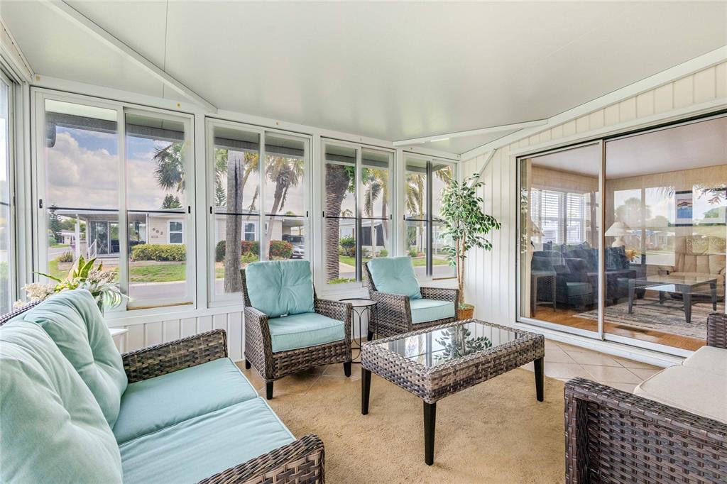 A sunroom with wicker furniture, light blue cushions, tile flooring, and large windows looking outside — 2100 KINGS HIGHWAY UNIT 683, PORT CHARLOTTE, FL
