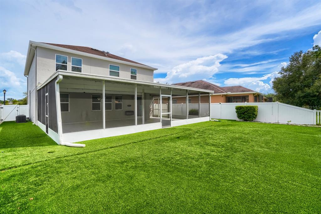 The exterior of a two-story house features a large screened-in patio and a grassy backyard — 3951 PACENTE LOOP, WESLEY CHAPEL, FL