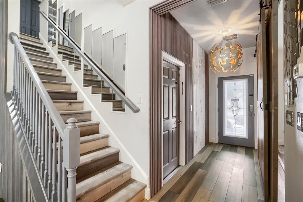 An entryway features a staircase with wood treads, a modern chandelier, and a paneled door — 3951 PACENTE LOOP, WESLEY CHAPEL, FL