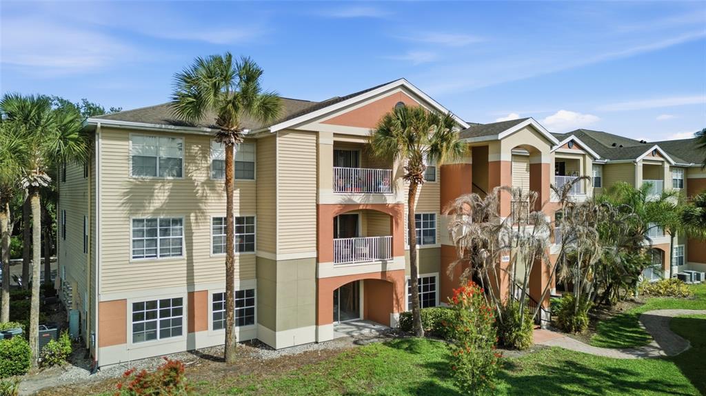 A three-story apartment building with tan siding, stucco accents, and palm trees in the foreground — 1950 SUMMER CLUB DRIVE UNIT 0214, OVIEDO, FL