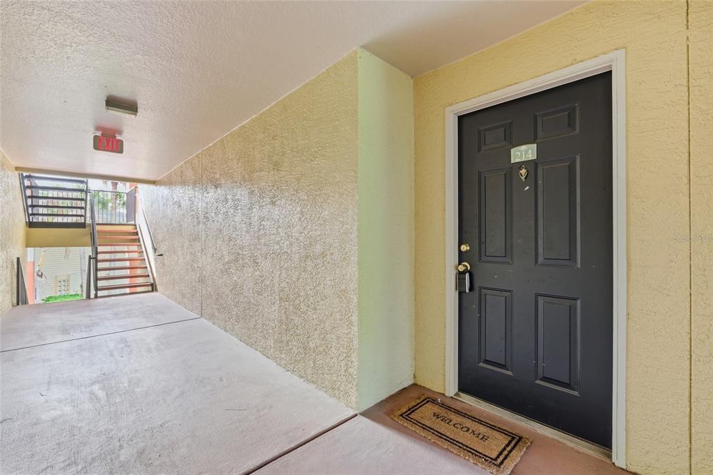 A dark gray apartment door with a welcome mat sits at the end of a hallway — 1950 SUMMER CLUB DRIVE UNIT 0214, OVIEDO, FL