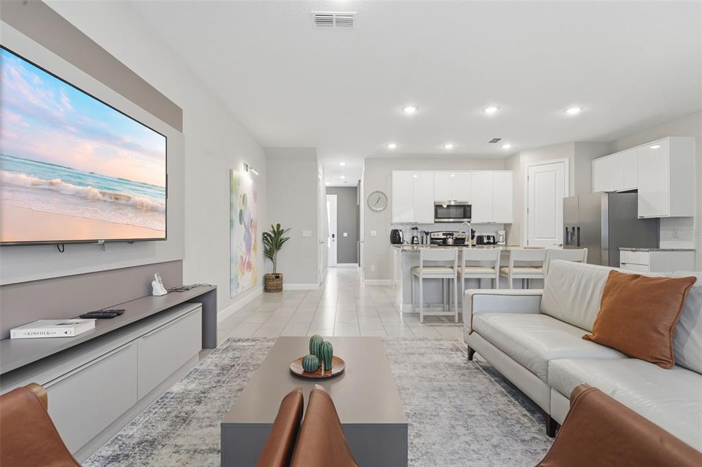 A modern open-concept living room features a large television, white cabinetry, and tile flooring — 7997 FORMOSA VALLEY PLACE, KISSIMMEE, FL