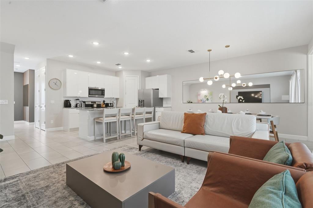 An open-concept living room and kitchen featuring white cabinetry, a sofa, and leather armchairs — 7997 FORMOSA VALLEY PLACE, KISSIMMEE, FL