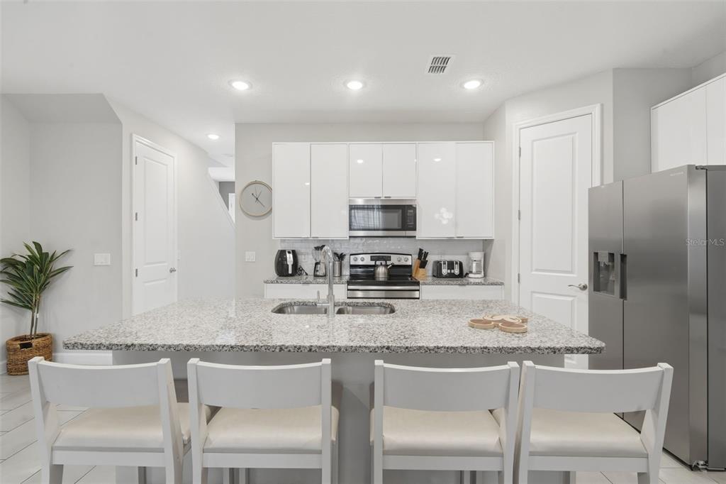 A modern kitchen features white cabinets, granite countertops, a central island, and stainless steel appliances — 7997 FORMOSA VALLEY PLACE, KISSIMMEE, FL