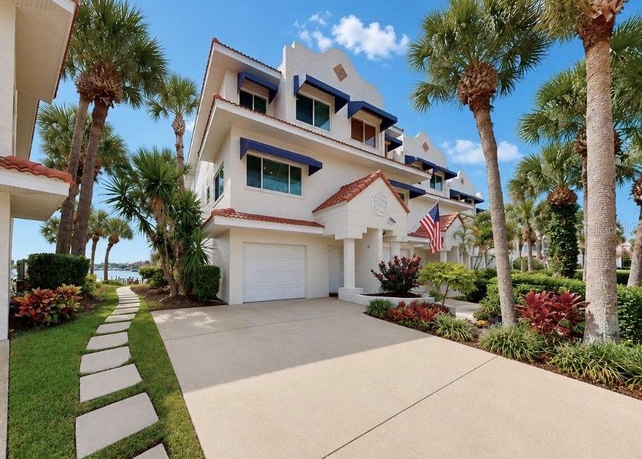 A three-story townhouse with a white exterior, blue awnings, and a concrete driveway — 4639 MIRABELLA COURT, ST PETE BEACH, FL
