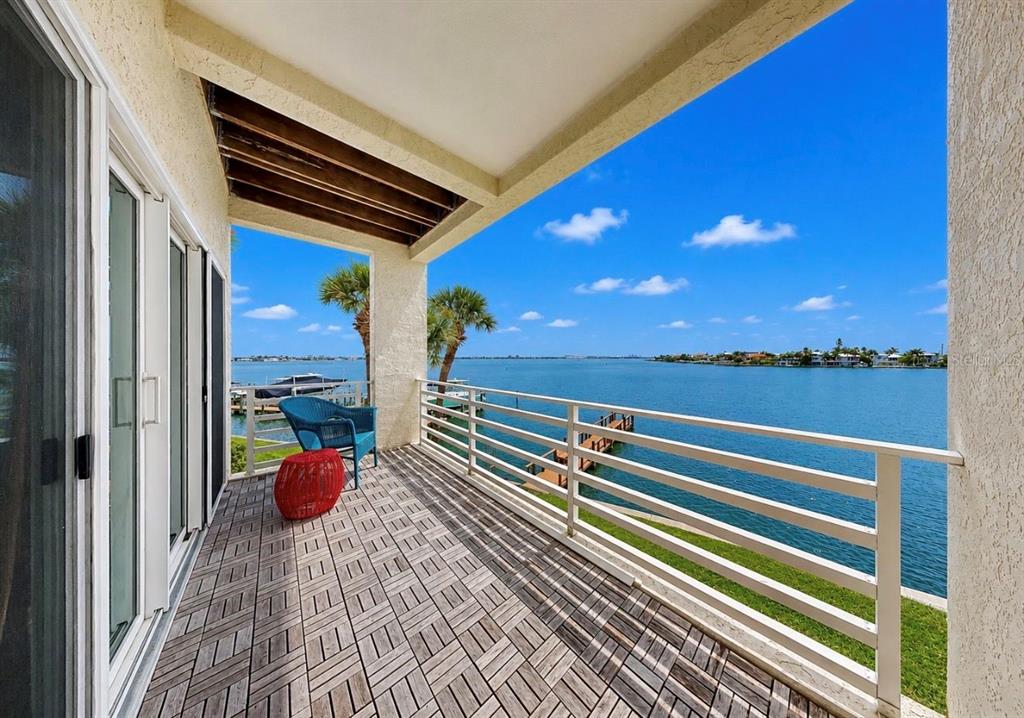 A balcony with wood-look tile flooring overlooks a body of water with a distant shoreline — 4639 MIRABELLA COURT, ST PETE BEACH, FL
